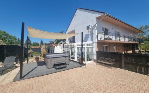 White two-story house with balcony, shade sail over a wooden deck, and a clear blue sky in the background, sunny day outdoor scene.