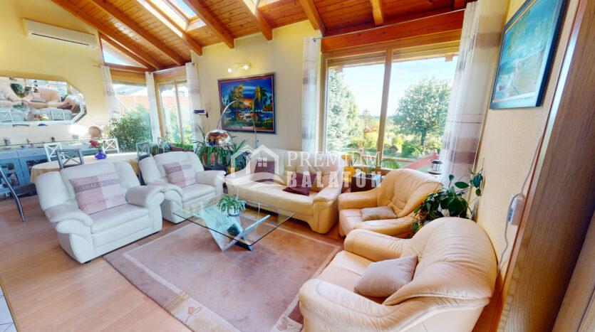Bright living room with cream leather sofas, glass coffee table, and large windows overlooking a garden outside.