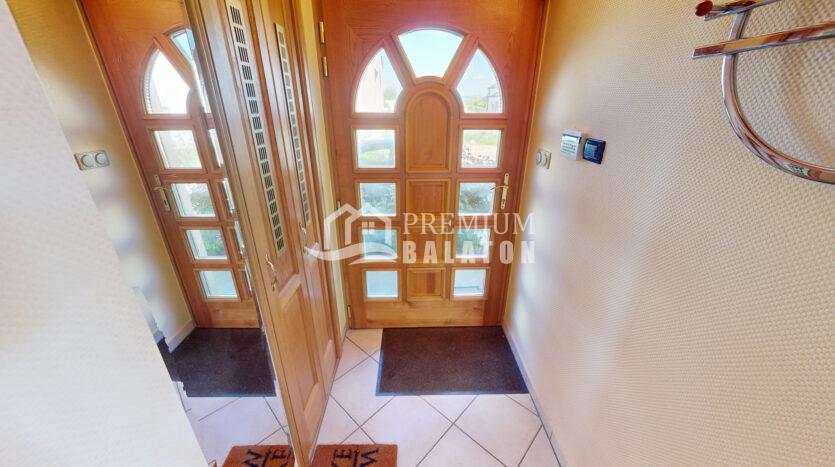 Wooden front door with many glass panes and an arched upper window, opening into a bright entryway with tiled floor and mats.