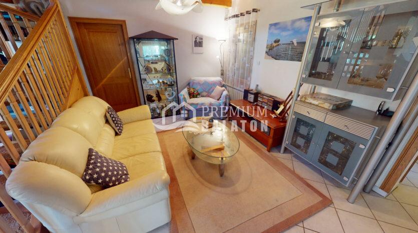 Cozy living room with a beige leather sofa, glass coffee table, staircase on the left, and a glass display cabinet.