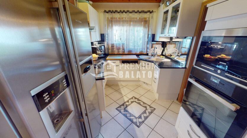 Modern stainless steel kitchen with a left refrigerator, built-in ovens, and a corner sink; watermark 'Premium Balaton' across the center.