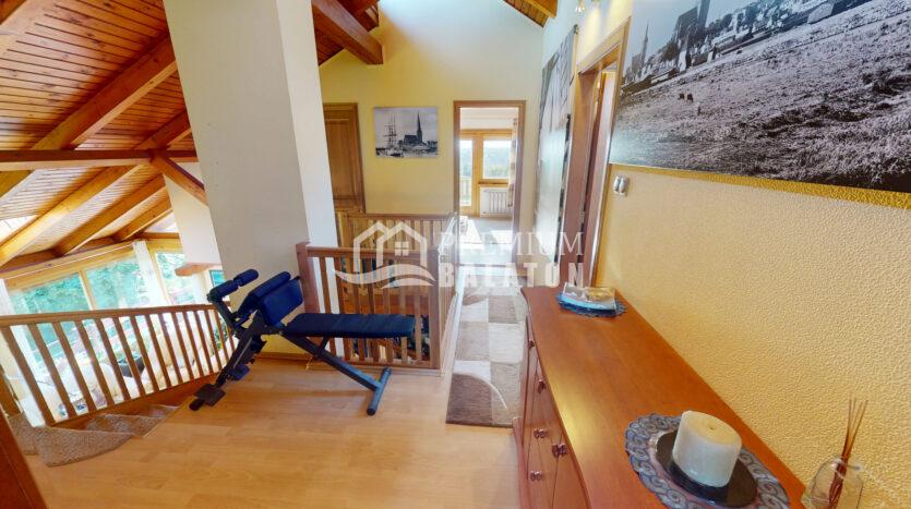 Loft hallway with cedar wood beams, a workout bench, and a railing along the upper staircase