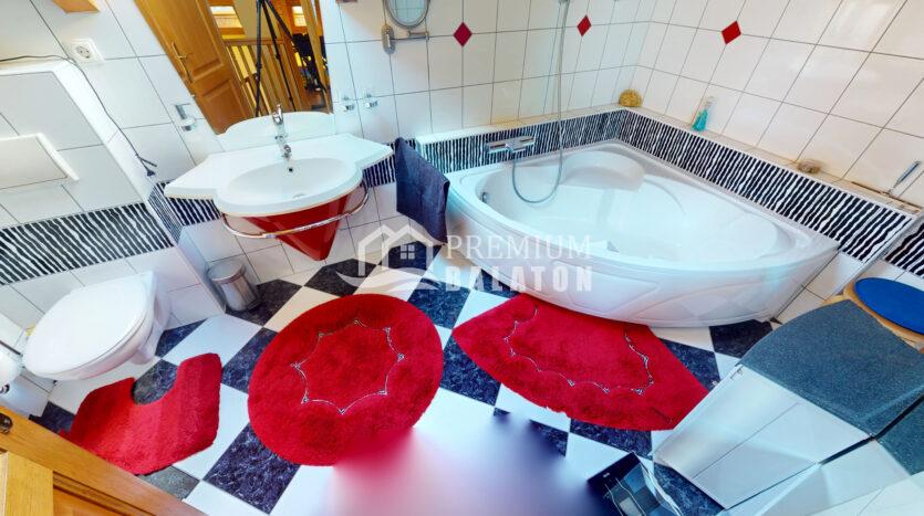 Bright bathroom with a white corner sink, chrome fixtures, a large curved bathtub, and black-and-white checkered floor topped by bold red circular rugs.