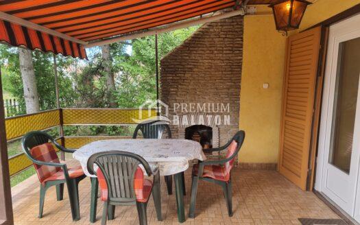 Outdoor patio with striped orange awning, brick grill, and yellow wall; tables and green chairs set for dining.