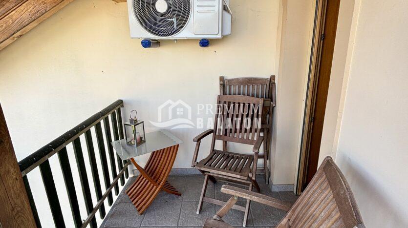 Small balcony with wooden chairs and a wall-mounted air conditioner beneath a wooden beam ceiling.