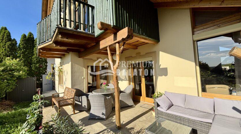Outdoor patio with wicker seating, wooden beams, and potted plants under a balcony of a modern home.