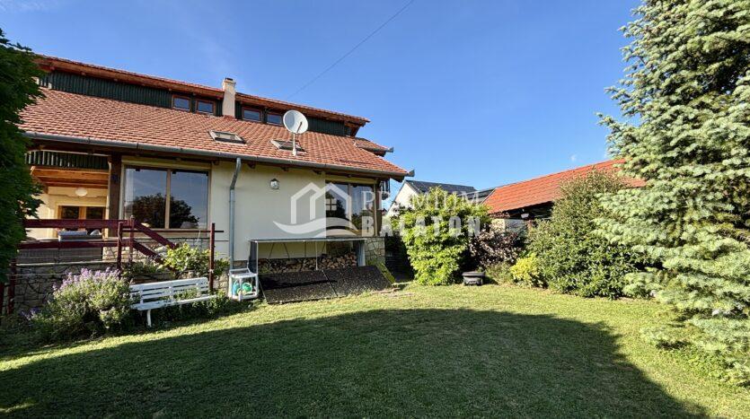 Two-story house with a red tile roof and satellite dish in a sunny garden setting.