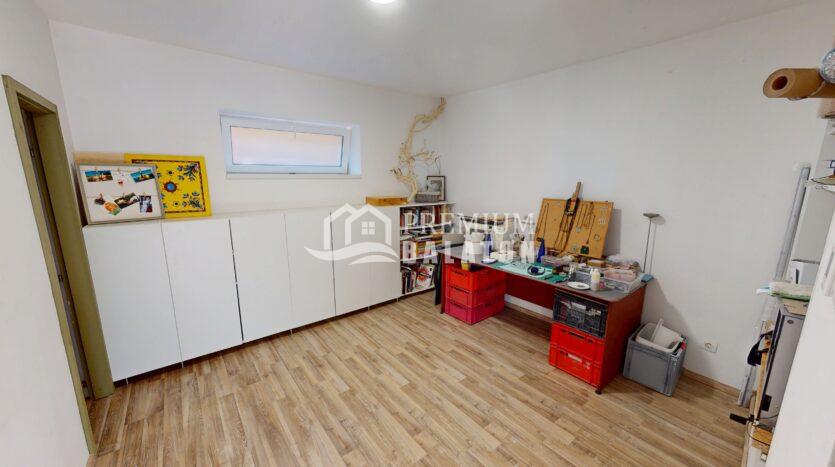 Bright workshop with white cabinets along the left wall, a small window, and a workbench with tools and jewelry displays.