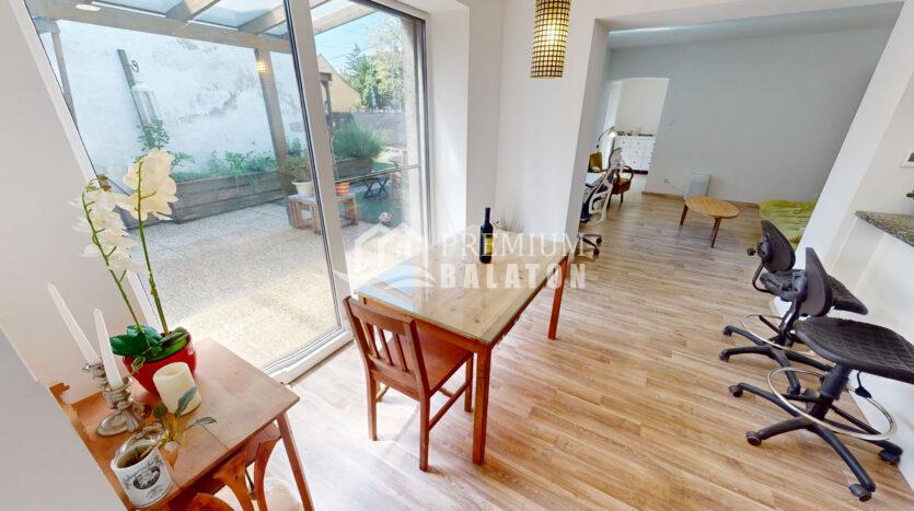 Bright open-plan living area with glass dining table and wooden chairs, facing a large glass door to a small garden patio.