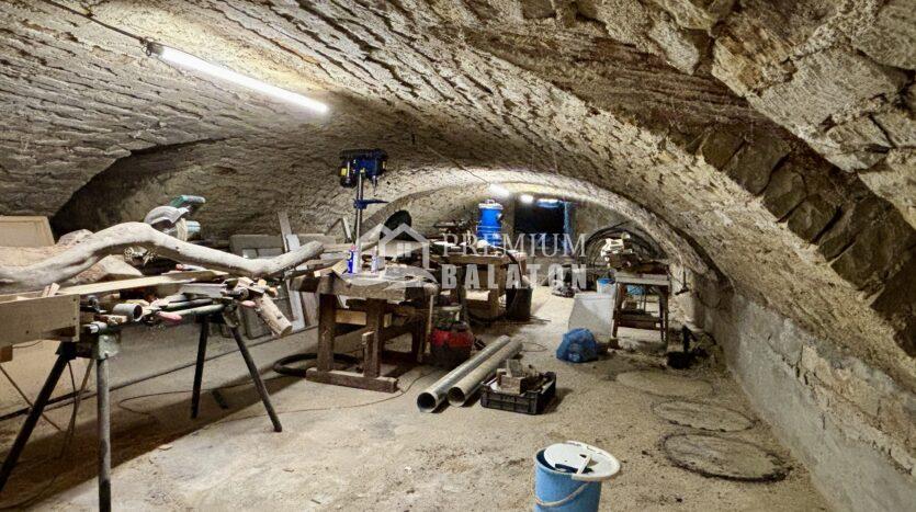 Underground tunnel workspace with rocky arched walls, scattered tools, pipes, and a blue barrel.