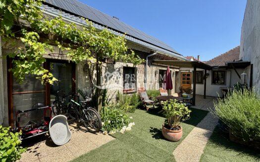 Backyard of a house with solar panels on the roof, greenery, and outdoor seating and bicycles nearby.