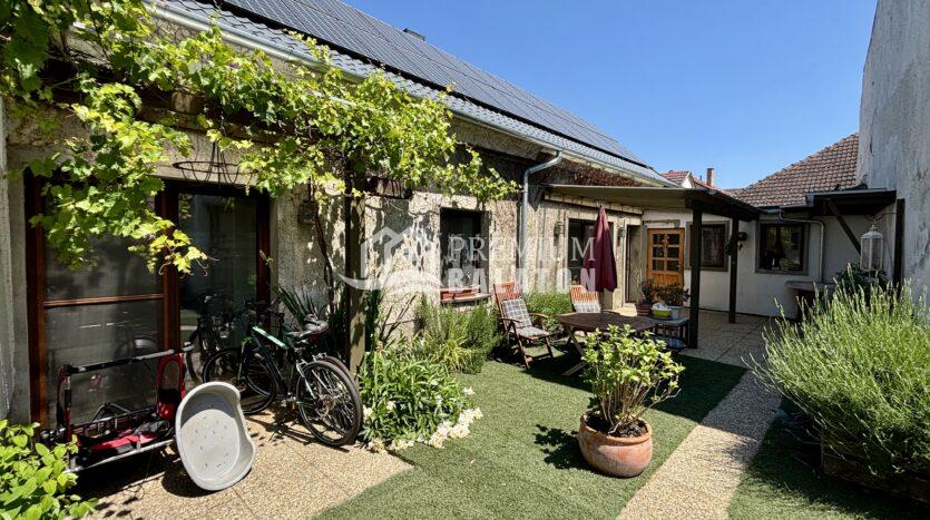 Backyard of a house with solar panels on the roof, greenery, and outdoor seating and bicycles nearby.