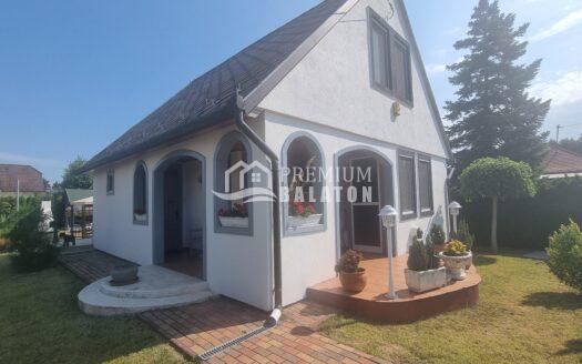 White house with a steep dark roof, arched porch openings, and a brick walkway in a sunny yard.
